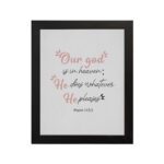 Psalm 115:3 Bible verse wall art with pink cursive and black text, floral accents, and a white background for a modern, spiritual design. hung on the wall in a black frame