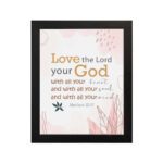 Love the Lord your God with all your heart, soul, and mind Matthew 22:37 Bible Wall Art with golden and black text, pastel pink abstract patterns, and leaf accents, displayed on the wall in a black frame in a white background