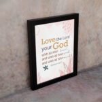 Love the Lord your God with all your heart, soul, and mind Matthew 22:37 Bible Wall Art with golden and black text, pastel pink abstract patterns, and leaf accents, displayed on the wall in a black frame