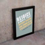 Rejoice always, pray without ceasing, give thanks in all circumstances 1 Thessalonians 5:16-17 Bible Wall Art with white and yellow text on muted teal background, bold design displayed on the wall in a black frame