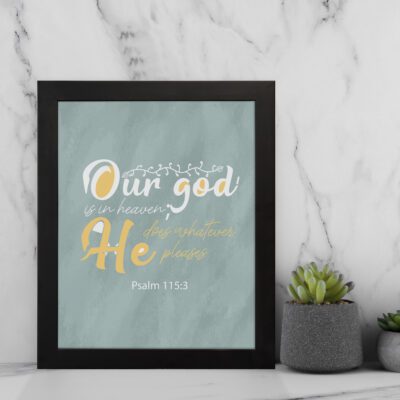 Christian wall art with Psalm 115:3 verse in gold and white text, set against a light sage green background, with elegant script fonts. displayed on the wall in a black frame