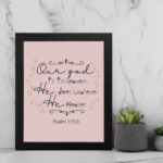 Psalm 115:3 Bible verse wall art with elegant black cursive text, vine decorations, and a soft pink background for a warm, spiritual design. displayed on the wall in a black frame