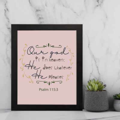 Psalm 115:3 Bible verse wall art with elegant black cursive text, vine decorations, and a soft pink background for a warm, spiritual design. displayed on the wall in a black frame