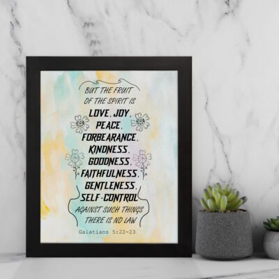 Fruit of the Spirit Bible verse wall art with black text and pastel watercolor background, Galatians 5:22-23. displayed on the wall in a black frame