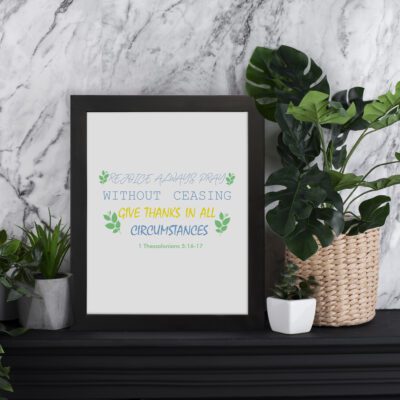 Rejoice always, pray without ceasing, give thanks in all circumstances 1 Thessalonians 5:16-17 Bible Wall Art with green leaf accents, white background, and black frame. displayed on the table