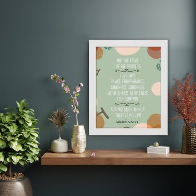 Christian wall art with Galatians 5:22-23 Bible verse on a light green background with light pink, brown, and green leaf design and white frame kept on a table