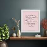 Psalm 115:3 Bible verse wall art with elegant black cursive text, vine decorations, and a soft pink background for a warm, spiritual design. displayed on the wall in a white frame