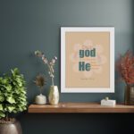 Psalm 115:3 Bible verse wall art with bold teal and orange text, blue highlights, and a soft beige background with a floral accent. displayed on the wall in a white frame