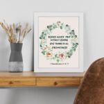 Rejoice always, pray without ceasing, give thanks in all circumstances 1 Thessalonians 5:16-17 Bible Wall Art with delicate floral wreath in pastel colors, light cream background displayed on the table