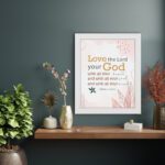 Love the Lord your God with all your heart, soul, and mind Matthew 22:37 Bible Wall Art with golden and black text, pastel pink abstract patterns, and leaf accents, displayed on the wall in a white frame