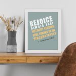 Rejoice always, pray without ceasing, give thanks in all circumstances 1 Thessalonians 5:16-17 Bible Wall Art with white and yellow text on muted teal background, bold design displayed on the table