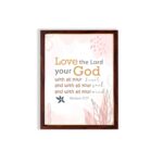 Love the Lord your God with all your heart, soul, and mind Matthew 22:37 Bible Wall Art with golden and black text, pastel pink abstract patterns, and leaf accents, displayed on the wall in a brown frame in a white background