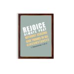 Rejoice always, pray without ceasing, give thanks in all circumstances 1 Thessalonians 5:16-17 Bible Wall Art with white and yellow text on muted teal background, bold design displayed on the wall in a brown frame in a white background