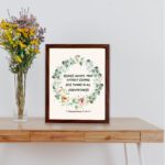 Rejoice always, pray without ceasing, give thanks in all circumstances 1 Thessalonians 5:16-17 Bible Wall Art with delicate floral wreath in pastel colors, light cream background in brown frame displayed on the table