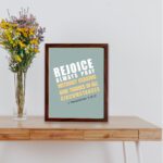 Rejoice always, pray without ceasing, give thanks in all circumstances 1 Thessalonians 5:16-17 Bible Wall Art with white and yellow text on muted teal background, bold design displayed on the table