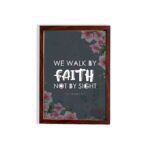 Christian wall art with 2 Corinthians 5:7 Bible verse on a light black background with a pink flower in the corner and white font and brown framed displayed on the wall