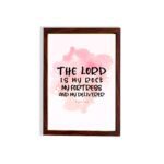 Bible wall art featuring The Lord Is My Rock, My Fortress, and My Deliverer in black handwritten-style lettering on a soft pink watercolor background. hung on the wall in a brown frame