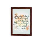 Christian wall art featuring the quote She is clothed with strength and dignity; she can laugh at the days to come from Proverbs 31:25, with an elegant design and pastel colors. hung on the wall in a brown frame