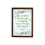 Christian wall art featuring Proverbs 31:25, with elegant script and floral accents in light green and gray background. hung on the wall in a brown frame