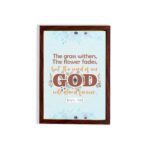 The Grass Withers Christian wall art with the verse Isaiah 40:8 in a modern font, featuring floral illustrations and a light blue background. hung the wall in a brown frame