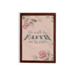 We Walk By Faith Not By Sight Christian Wall Art with pink roses and gray leaves on a soft pink background hung on the wall in a brown frame.