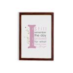 Christian wall art featuring the phrase 'I Still Remember The Days I Prayed For What I Have Now' with pink and gray text and gold flowers. hung on the wall in a brown frame