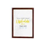 Christian wall art featuring the phrase Your Right Hand Upholds Me in playful fonts with a yellow cursive style and decorative waves. hung on the wall in a brown frame