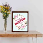 Beautiful wall art with the quote Because your love is better than life from Psalm 63:3, featuring a floral design on a light blue background. displayed on the table in a brown frame