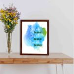 Bible wall art featuring the phrases Start With Jesus, Stay With Jesus, and End With Jesus in cursive on a watercolor blue and green background. displayed on the table in a brown frame