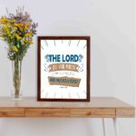 Bible wall art featuring The Lord Is My Rock, My Fortress, and My Deliverer in blue and tan text on a white background with decorative lines. displayed on the table in a brown frame