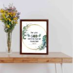 Wall art featuring the quote With God Nothing Shall Be Impossible from Luke 1:37, surrounded by a golden frame and green leaves. displayed on the table in a brown frame