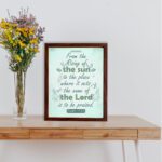 Wall art displaying Psalm 113:3 with elegant cursive font and leafy motifs on a mint green background. displayed on the table in a brown frame