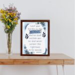 Christian wall art featuring Psalm 55:22 with navy blue text on a light blue and white background, decorated with blue flowers. displayed on the table in a black frame