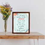 Cast Your Burden on the Lord Psalm 55:22 Christian wall art with teal and coral text on a mint green background with floral accents. displayed on the table in a brown frame