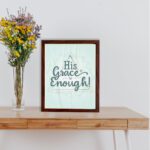 His Grace Is Enough Bible wall art with a mint background and teal script design, surrounded by decorative elements. displayed on the table in a brown frame