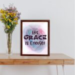 His Grace Is Enough Christian wall art with bold dark purple text and a soft gradient background in pink, purple, and blue. displayed on the table in a brown frame