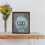 Isaiah 40:8 Christian wall art with light gray and white text on a muted blue background, featuring "GOD" in bold letters. displayed on the table in a brown frame