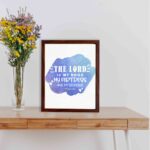 Bible wall art with The Lord Is My Rock, My Fortress, and My Deliverer in white stencil-style text on a blue watercolor background. displayed on the table in a brown frame