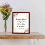 Infidu Bible wall art with Colossians 3:2 in dark brown text, surrounded by peach and beige flowers on a cream background. displayed on the table in a brown frame