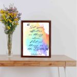 Bible wall art featuring Colossians 3:2 in cursive text on a colorful rainbow background. displayed on the table in a brown frame