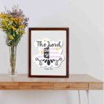 Bible wall art with The Lord Is My Rock, My Fortress, and My Deliverer in colorful pastel text on a light grey background with decorative elements. displayed on the table in a brown frame