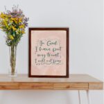 Wall art featuring the quote In God I Have Put My Trust I Will Not Fear from Psalm 56:4 in a bold, playful font. displayed on the table in a brown frame