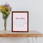 Christian wall art with the quote from Proverbs 2:6, featuring the word "Wisdom" in script on a soft pink background. displayed on the table in a brown frame