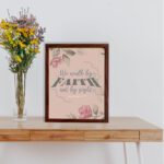 We Walk By Faith Not By Sight Christian Wall Art with pink roses and gray leaves on a soft pink background displayed on the table in a brown frame.