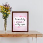 Christian wall art displaying We Walk By Faith Not By Sight with floral elements on a pale pink background. displayed on the table in a brown frame