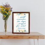 Christian wall art with the quote I Still Remember The Days I Prayed For What I Have Now surrounded by floral decorations. displayed on the table in a brown frame