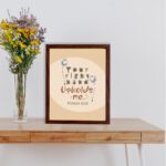 Christian wall art with the phrase "Your Right Hand Upholds Me" Psalm 63:8, featuring bold text and floral accents on a peach background. displayed on the table in a brown frame