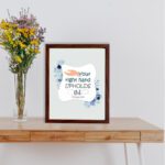 Your Right Hand Upholds Me Psalm 63:8 Christian wall art with a hand illustration and floral accents on a light gray background. displayed on the table in a brown frame