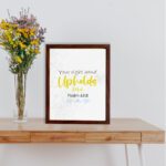 Christian wall art featuring the phrase Your Right Hand Upholds Me in playful fonts with a yellow cursive style and decorative waves. displayed on the table in a brown frame