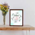 Proverbs 4:7 Bible verse wall art with green leaf wreath and red flowers, perfect for Christian home decor. displayed on the table in a brown frame